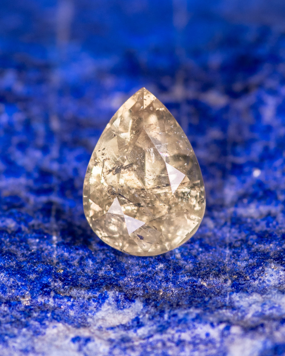 1.90 carat green yellow sapphire resting on vivid blue textured background, highlighting internal reflections and brilliance of its modified pear cut, untreated gemstone from Umba River Valley, Tanga, Tanzania.