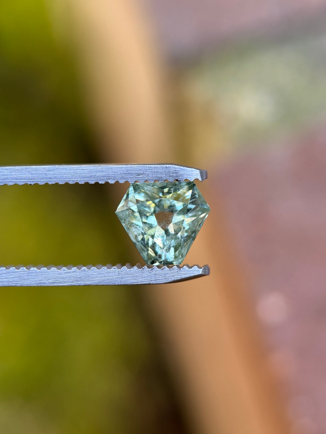 Mint teal green Montana sapphire held in gem tweezers, highlighting antique style cut corner trillion shape, crisp facet symmetry, and natural untreated sapphire