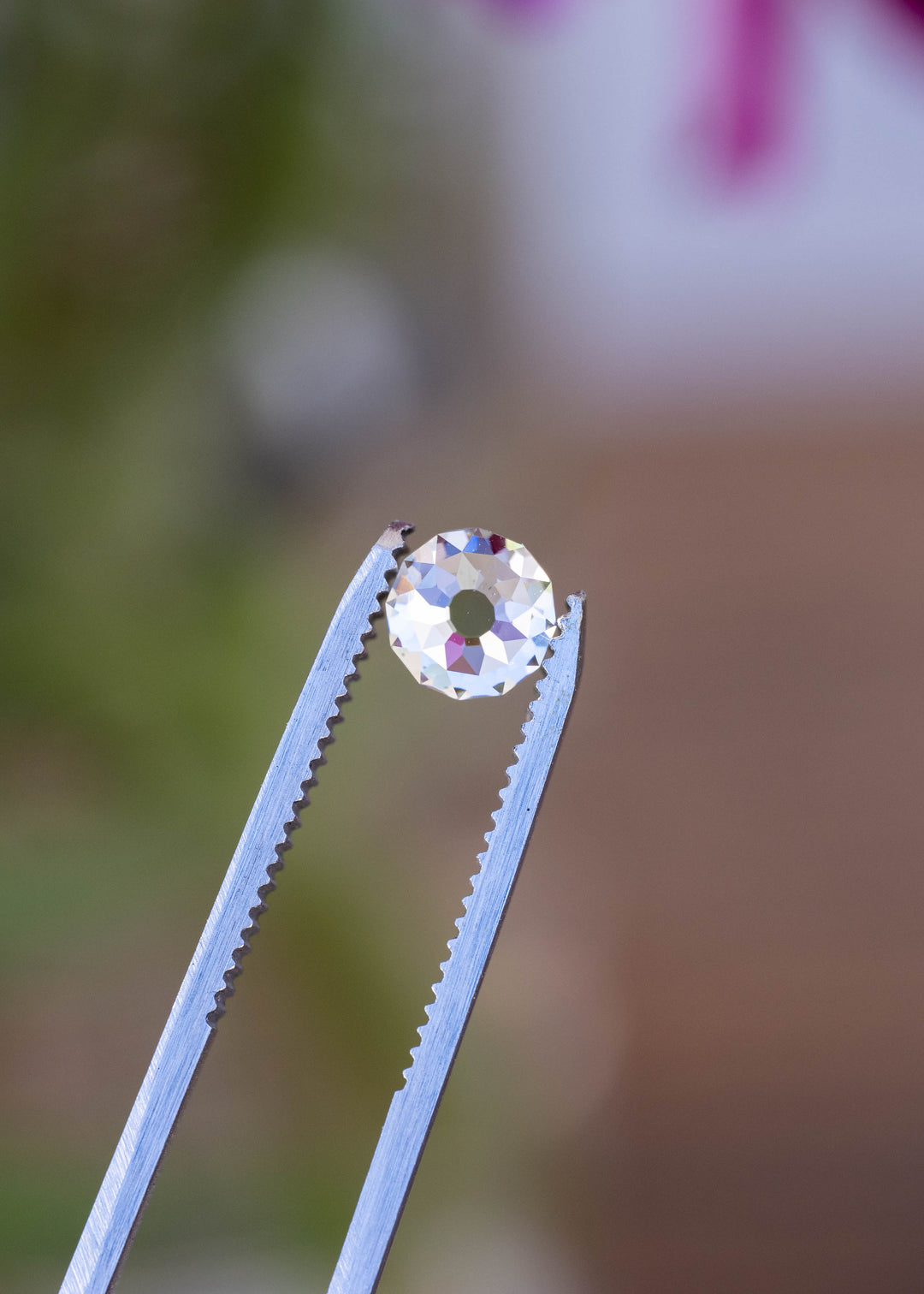 1.92 carat round Mughal cut South African diamond held in jeweler’s tweezers against a softly blurred natural background, showing its circular outline and open table.