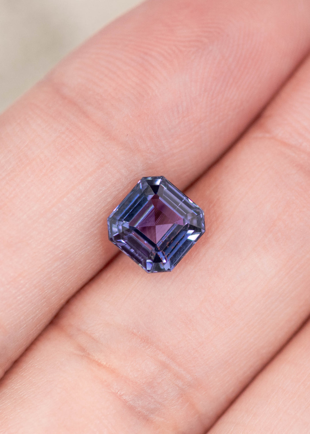 1.93 carat blue violet Tanzanite Asscher cut resting on finger, precision faceted square step cut gemstone from Tanzania highlighting geometric facet pattern, depth and vibrant color for bespoke jewelry