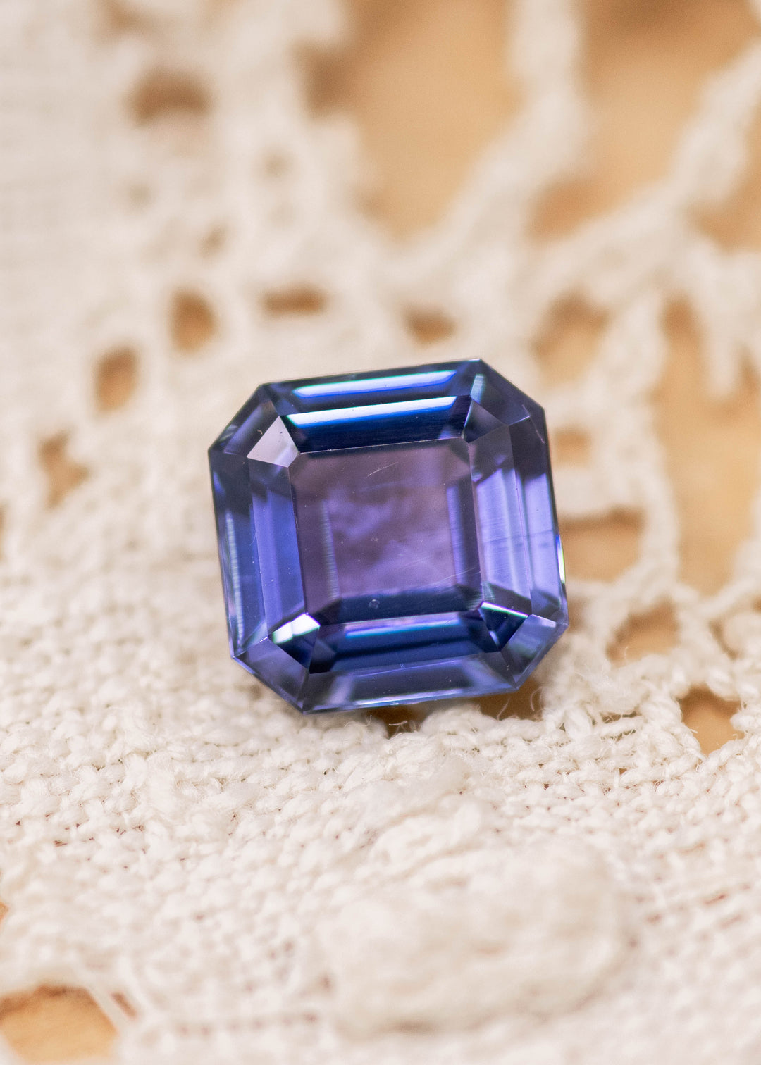 1.93 carat blue violet Tanzanite Asscher cut gemstone displayed on fabric surface, precision step cut stone from Merelani Hills Tanzania showing crisp facets, symmetry and rich violet blue color for custom jewelry