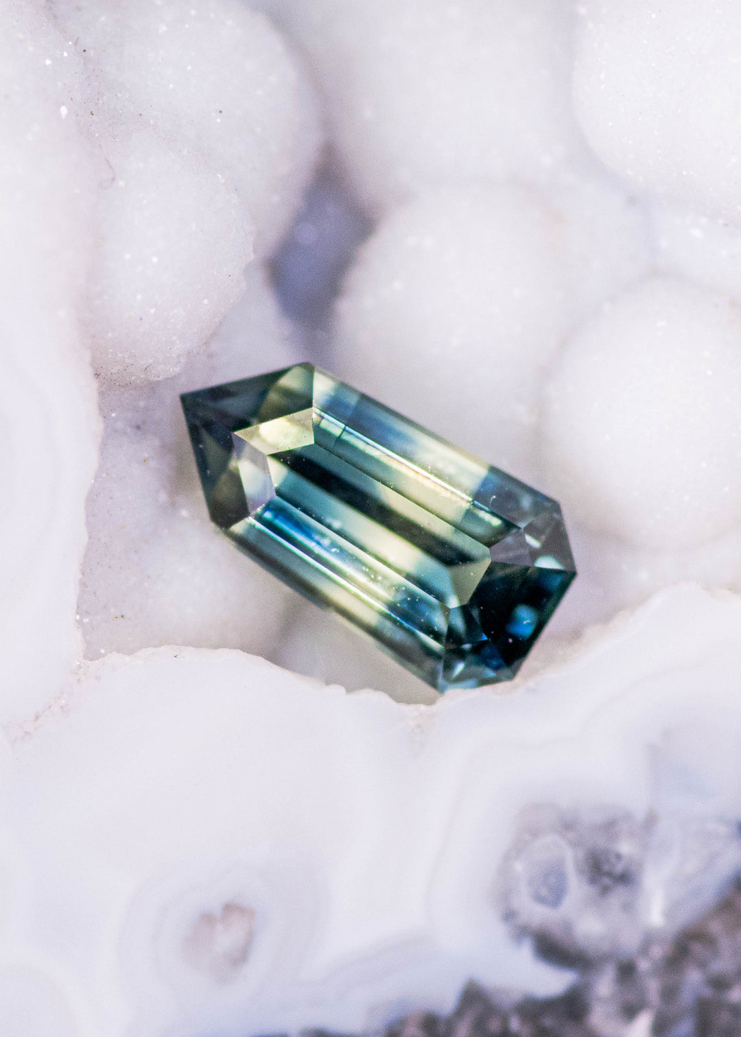 Loose bi-color yellow blue green sapphire from Diego Madagascar resting on a crystal surface showing the custom modified step cut shield shape and natural color zoning.