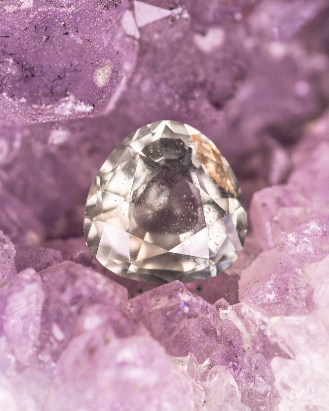 1.94 carat yellow teal green sapphire nestled in purple amethyst crystals, capturing the natural brilliance and clarity of this untreated custom portrait pear cut gemstone from Umba River, Tanzania.