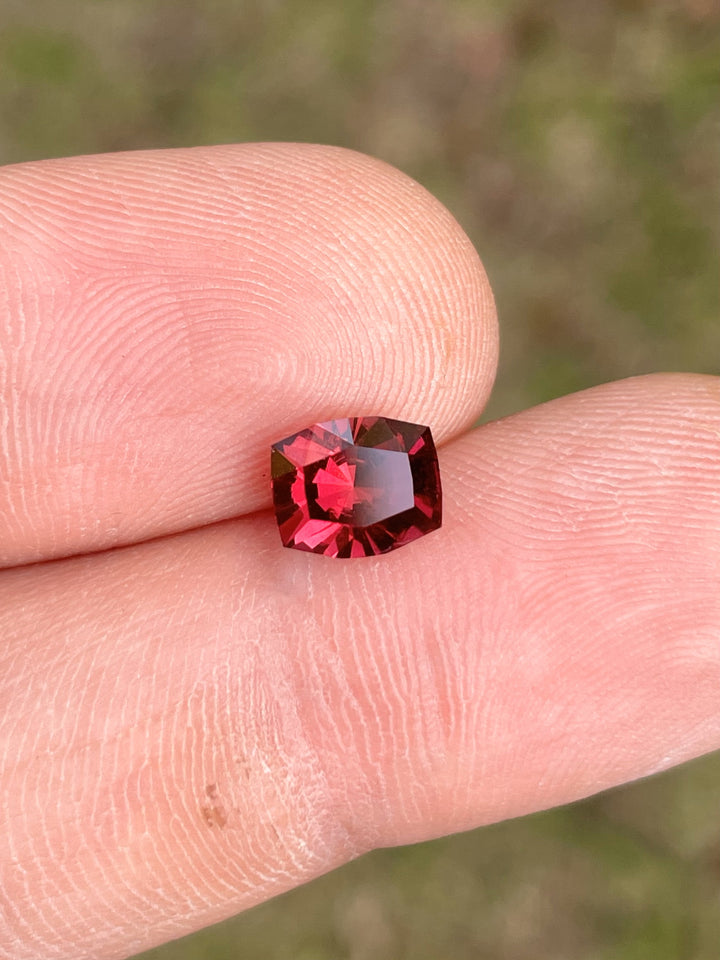 Close-up of a vibrant red-purple garnet, featuring a 1.97 carat cushion brilliant cut with exceptional clarity and brilliance.