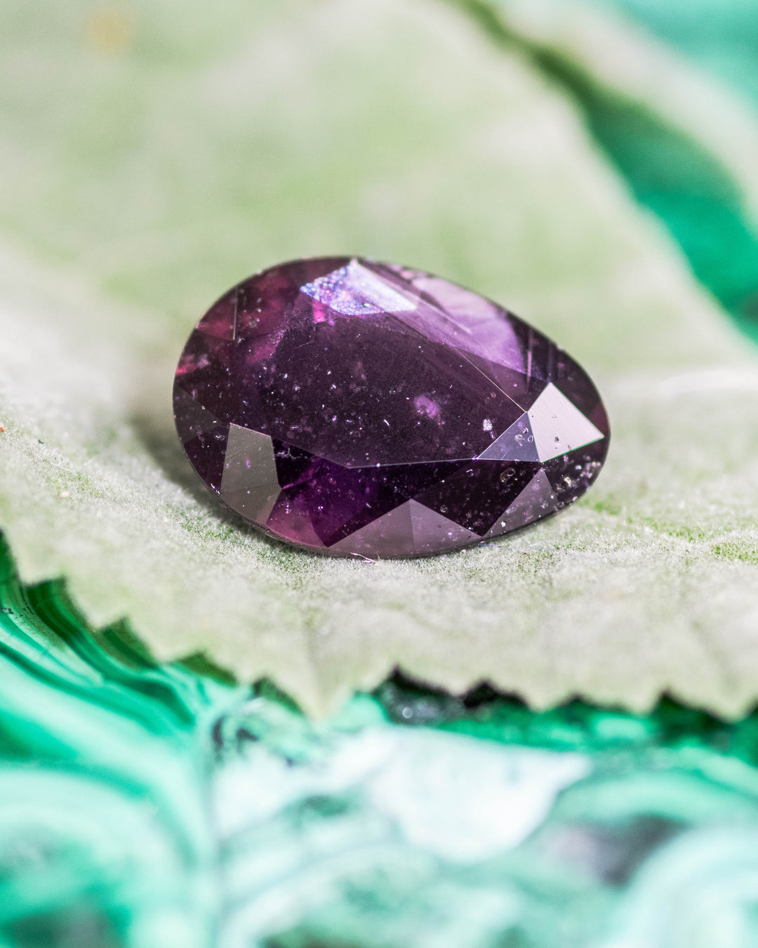 1.98 carat plum purple sapphire resting on a soft green leaf, showcasing its deep violet reflections and fine clarity in a modified tear drop cut, untreated gemstone from Umba River, Tanzania