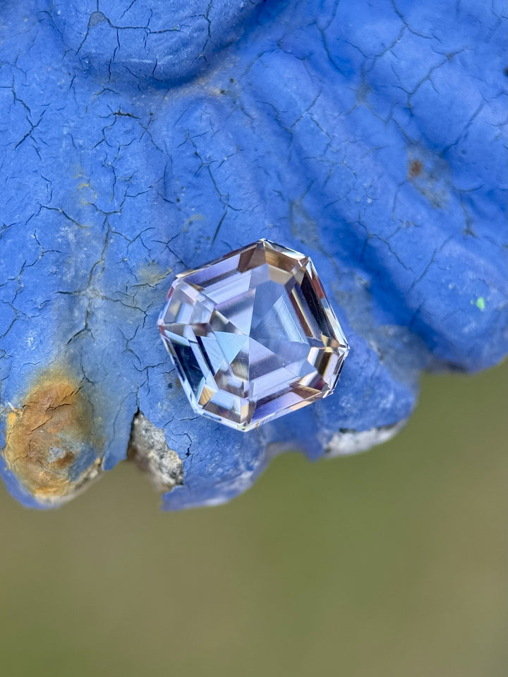 1.99 carat Tanzanite in custom Asscher cut placed on textured blue surface, displaying pastel yellow, lavender, and teal hues
