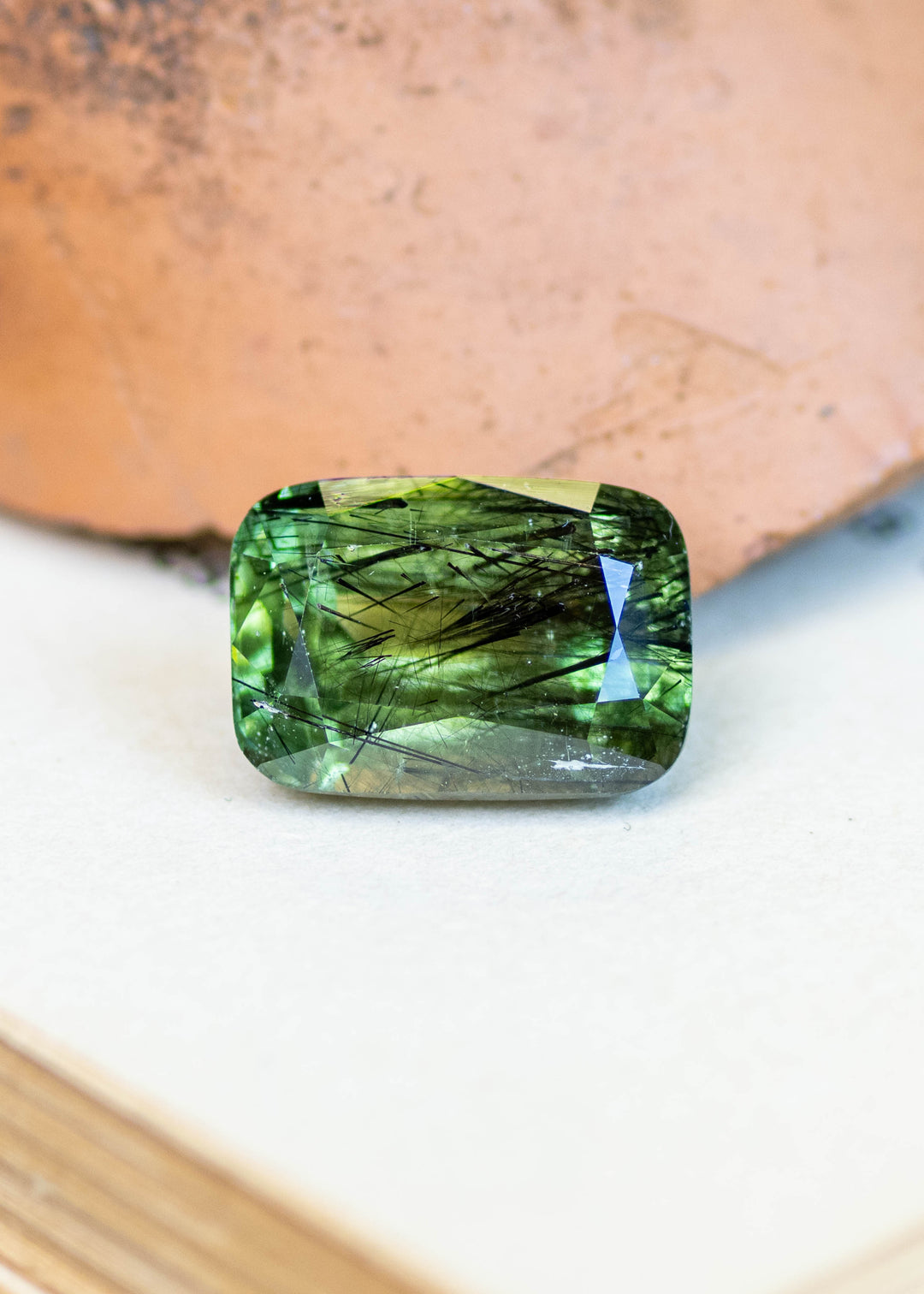 Natural untreated 10.89 carat forest green peridot from Pakistan displayed in natural light, featuring a modified radiant cut and striking natural needle inclusions.