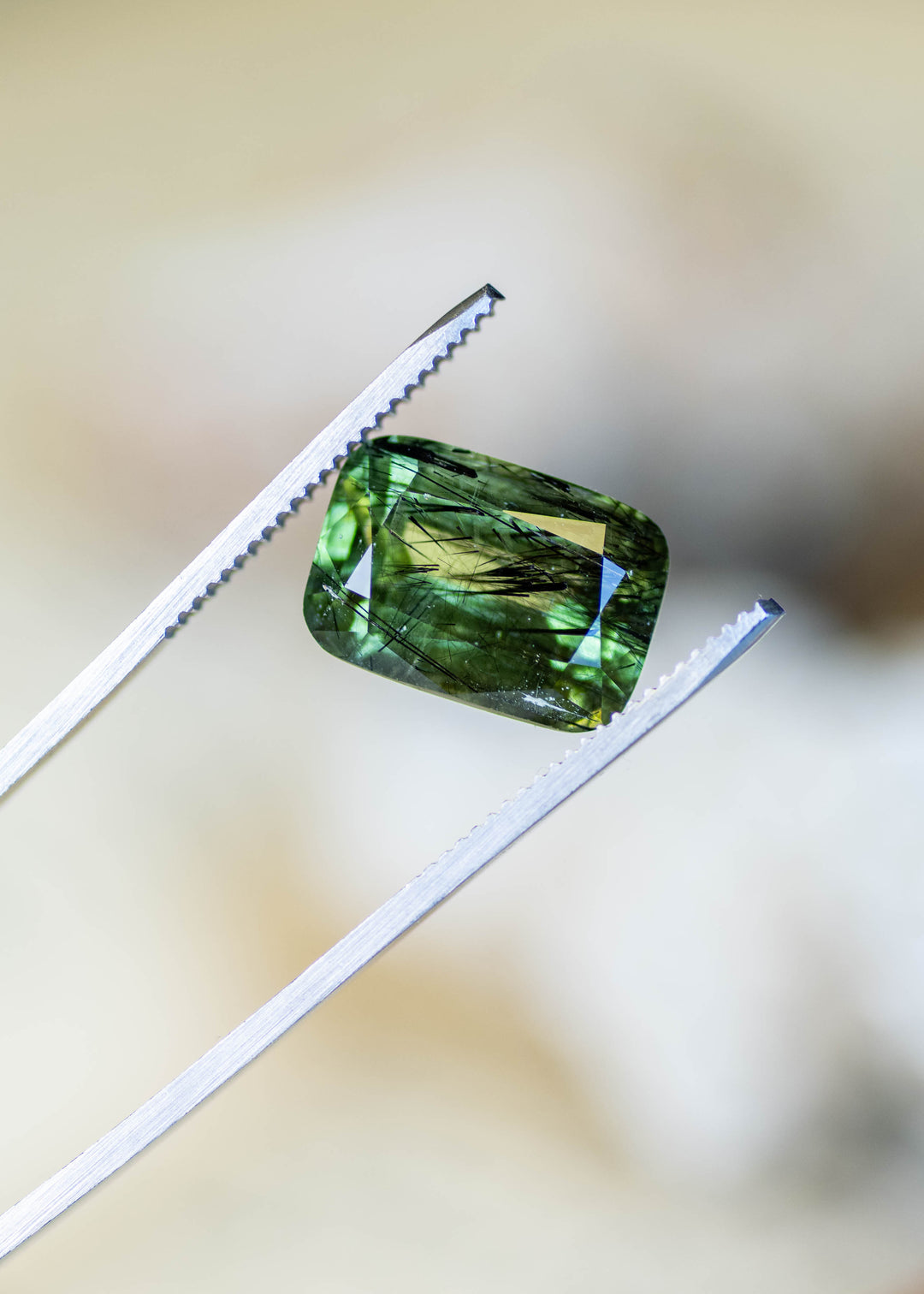 Close-up of a natural Pakistani forest green peridot in tweezers, highlighting its modified radiant cut, vivid internal reflections, and dramatic natural inclusions.