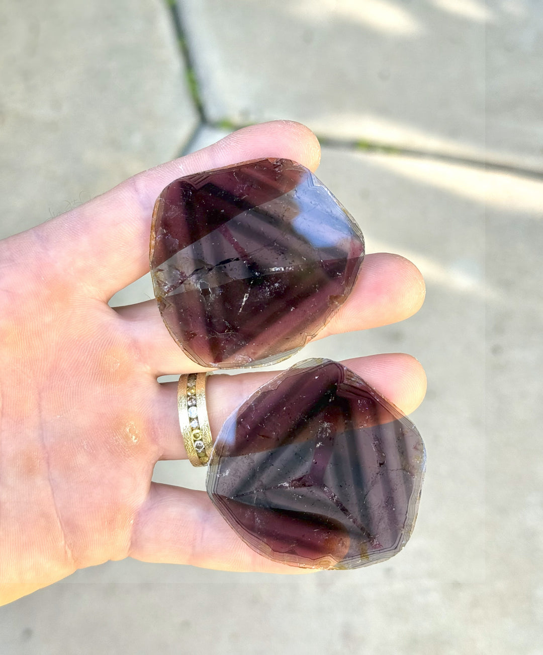 Pair of 123.90 carat liddicoatite tourmaline crystals held in sunlight, showcasing vivid internal triangular zoning and multicolor layers of pink, blue, and purple, sourced from Madagascar.