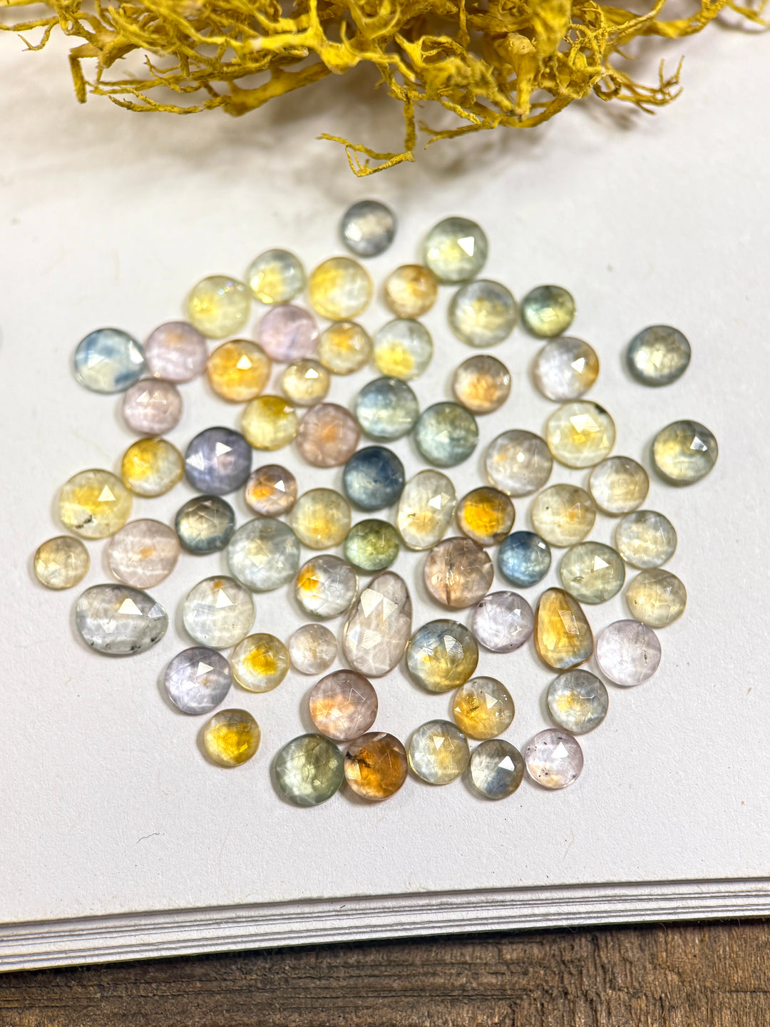 Parcel of 66 fancy parti sapphires in teal, blue, green, yellow, orange, purple, and pink tones from the Eldorado Deposit, Montana. Each gemstone shows distinct color zoning and sparkle from its mixed round, oval, and freeform cuts, totaling 17.40 carats and heat-treated for enhanced brilliance.