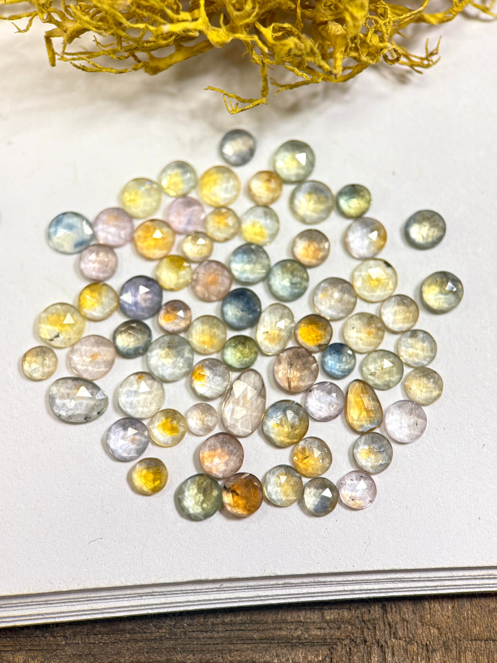 Parcel of 66 fancy parti sapphires in teal, blue, green, yellow, orange, purple, and pink tones from the Eldorado Deposit, Montana. Each gemstone shows distinct color zoning and sparkle from its mixed round, oval, and freeform cuts, totaling 17.40 carats and heat-treated for enhanced brilliance.