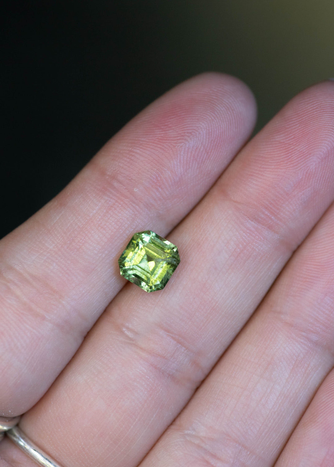 Untreated 2.81 carat lime green peridot from Pakistan displayed on fingertips for scale, featuring a custom Asscher cut and vibrant natural brilliance.