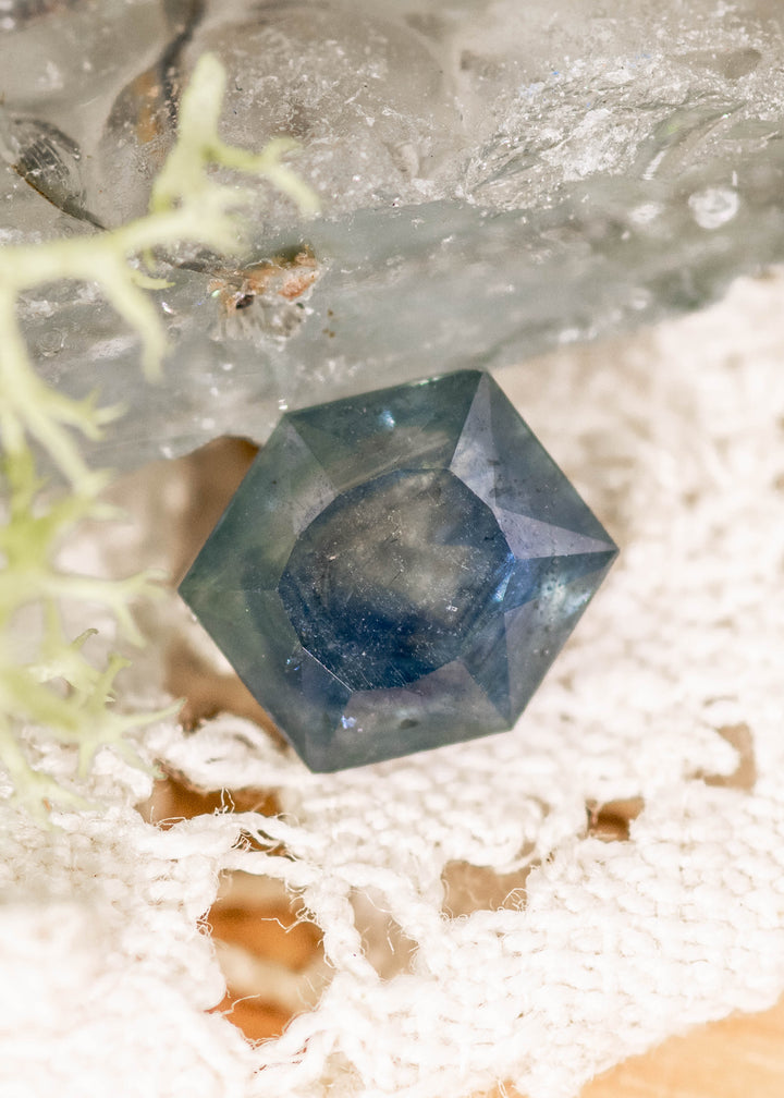 2.00 carat untreated Montana sapphire in teal blue gradient hexagonal brilliant tablet cut displayed on lace with natural crystal background, showing geometric faceting and color zoning from El Dorado Bar Deposit USA