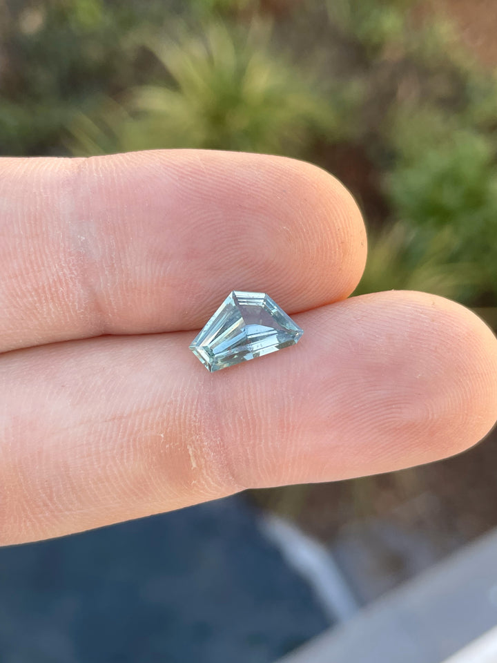 Close-up of a 2.00-carat sapphire with a geometric freeform cut in blue and green hues, resting on a fingertip.