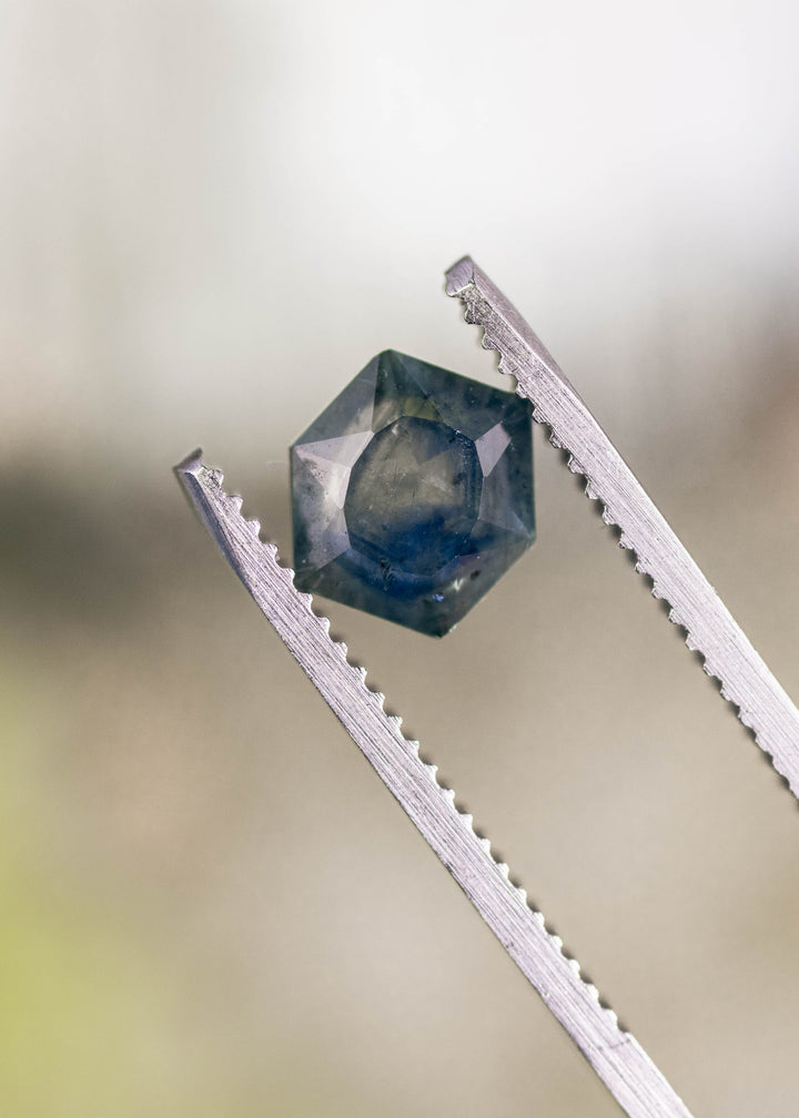 2.00ct teal blue gradient Montana sapphire held in gem tweezers, hexagonal brilliant tablet cut with precision facets visible, untreated stone from El Dorado Bar Deposit Montana USA