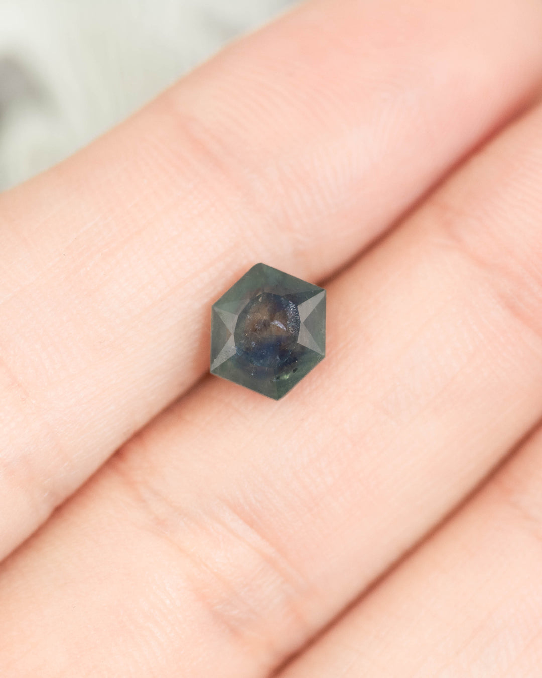 Close-up of 2.00 carat hexagonal brilliant tablet cut Montana sapphire resting on hand, showing teal to blue gradient color and untreated clarity from El Dorado Bar Deposit USA