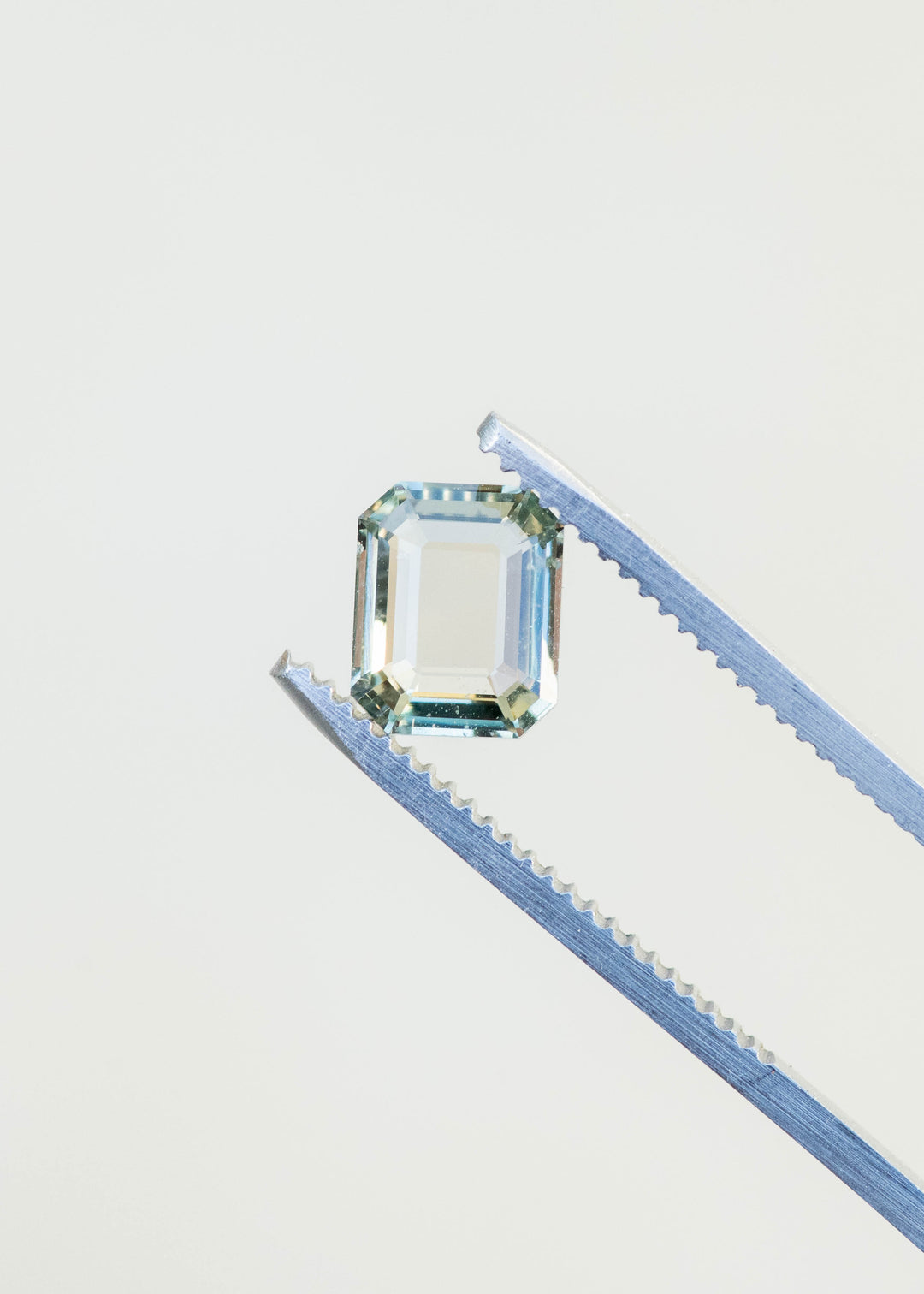 Mint green sapphire held in gem tweezers showcasing clarity and soft green tone.