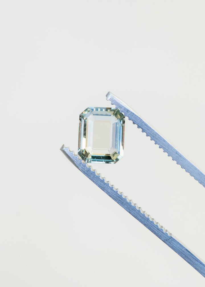 Mint green sapphire held in gem tweezers showcasing clarity and soft green tone.