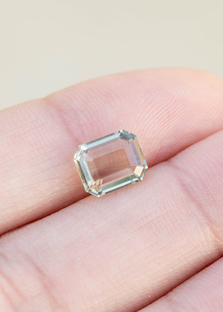 Mint green portrait cut sapphire held in fingertips under natural lighting.