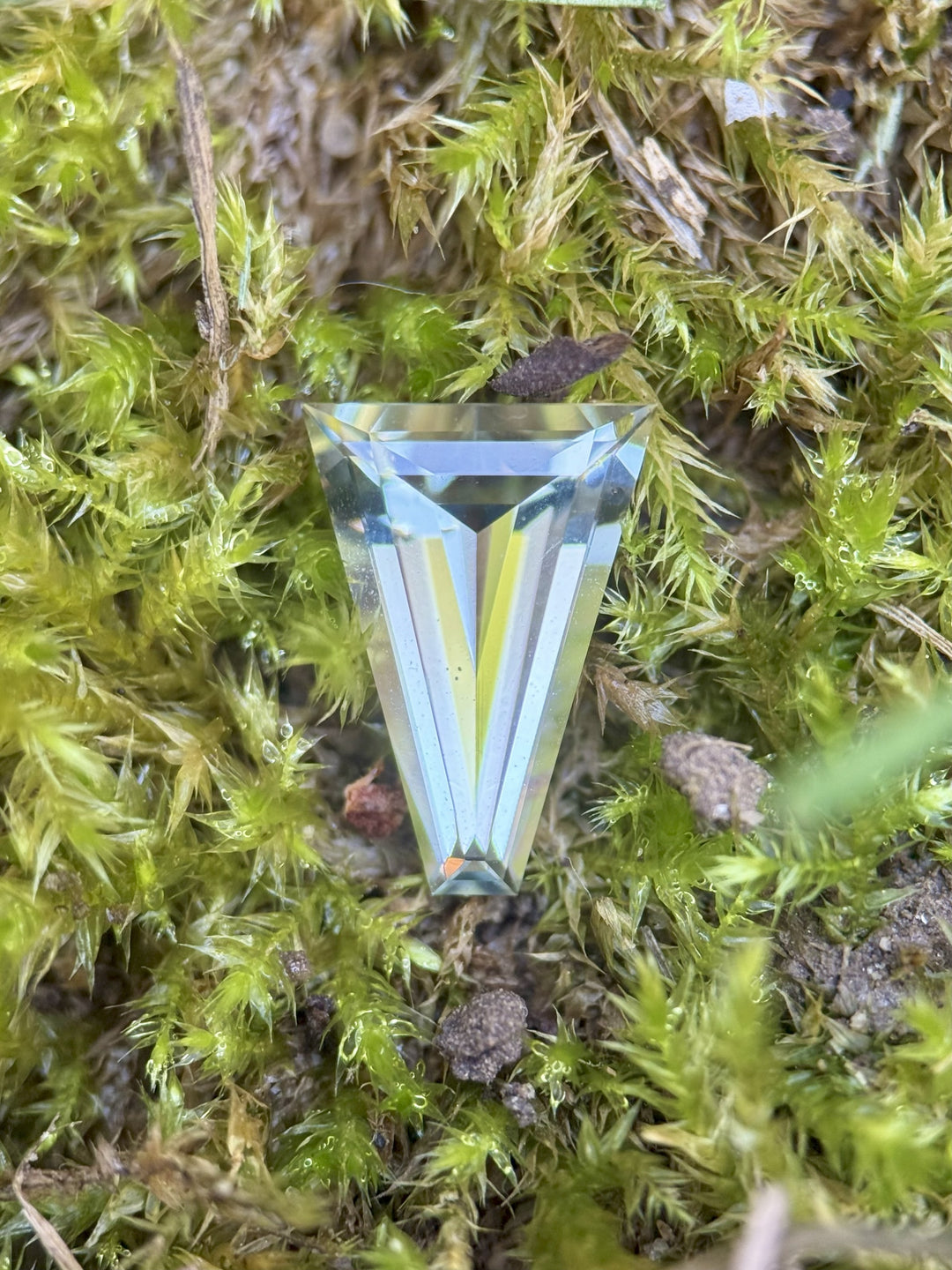 2.02 carat mint green tourmaline resting on bright green moss, showcasing its tapered baguette step cut and natural luster, untreated gemstone ethically sourced from Congo, Africa.