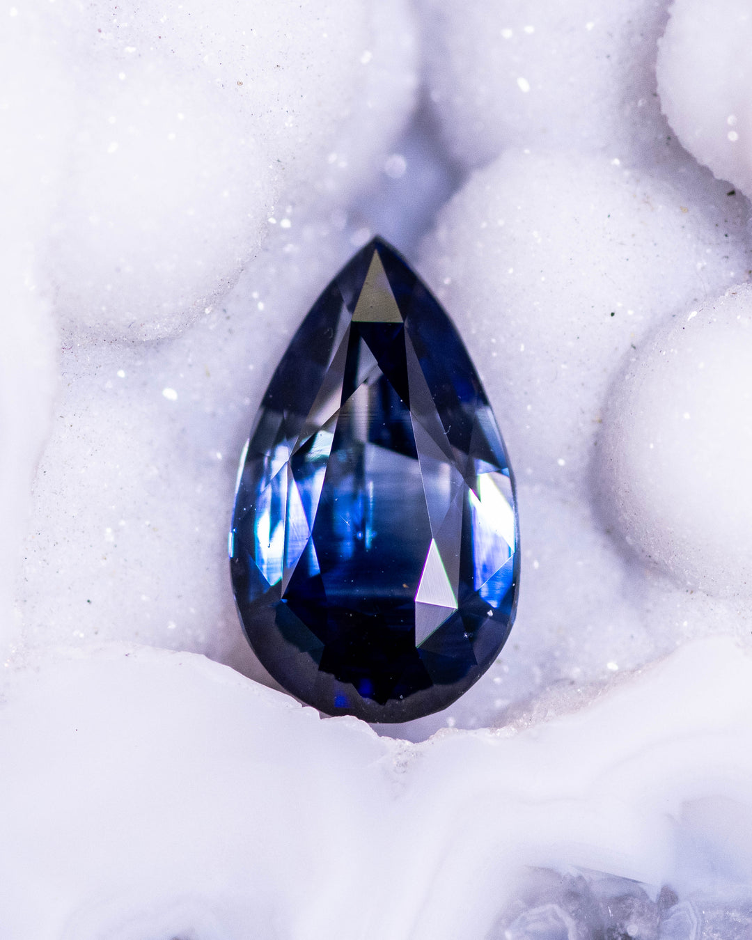 2.02 carat bi-color blue sapphire resting in a white crystalline geode, highlighting the rich blue tones and precise symmetry of its pear brilliant cut, untreated gemstone from Sakaraha, Madagascar.