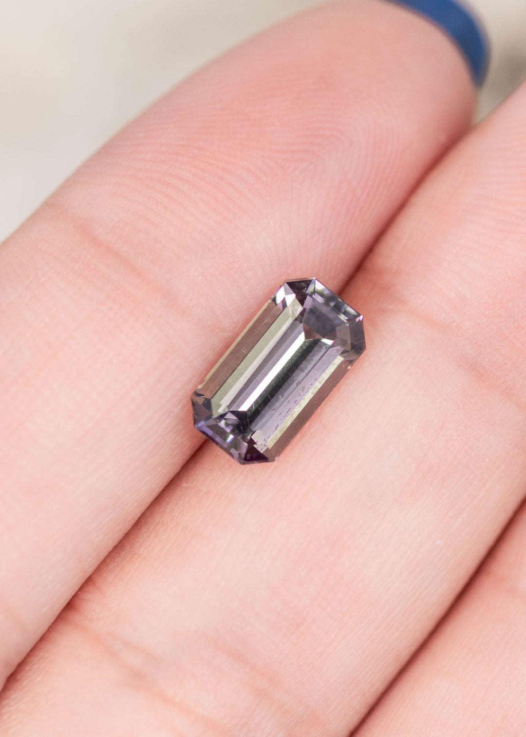 2.02 carat purple green Tanzanite emerald cut gemstone resting on finger, untreated Merelani Hills Tanzania stone showing step cut faceting, natural color shift and clarity for custom fine jewelry