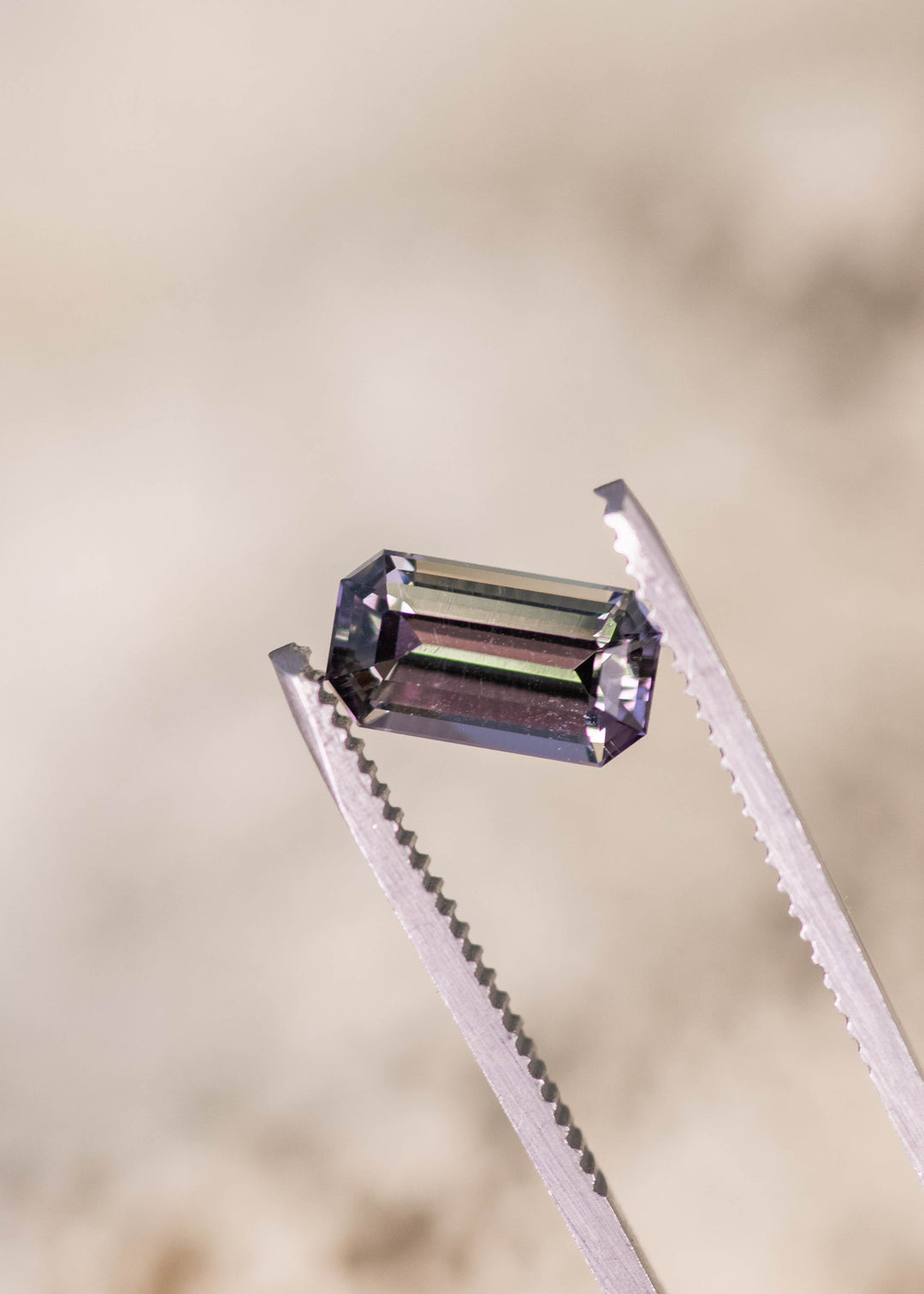 2.02 carat purple green Tanzanite emerald cut held in tweezers, untreated gemstone from Merelani Hills Arusha Tanzania displaying clean step facets, brilliance and precision cut for custom jewelry design