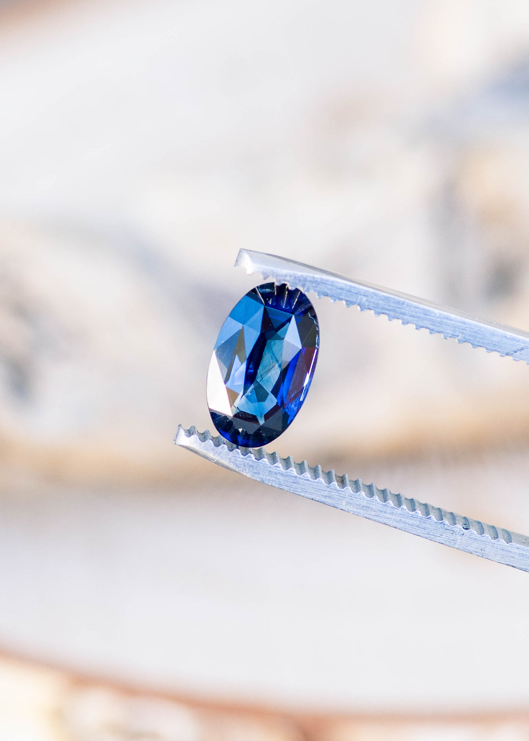 2.02ct deep blue elongated moval cut sapphire from madagascar held in gem tweezers under natural lighting.
