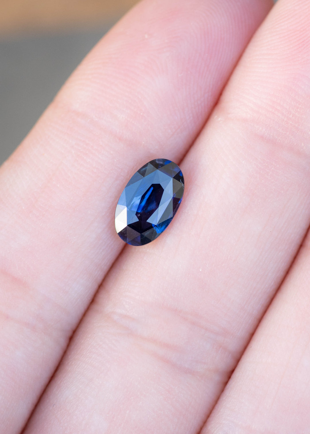 2.02ct deep blue elongated moval cut sapphire from madagascar held in fingertips to show color and scale.