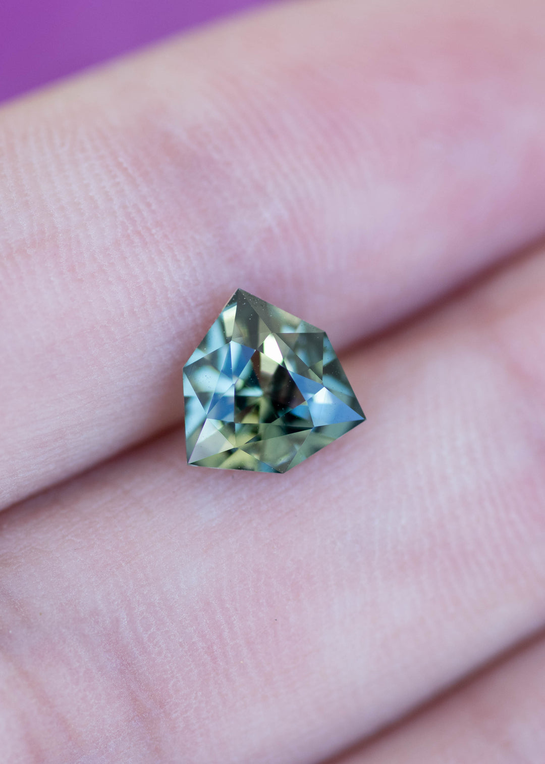 Loose 2.03 carat bluish teal green parti sapphire shown on hand highlighting size, brilliance, and unique shield-shaped faceting.