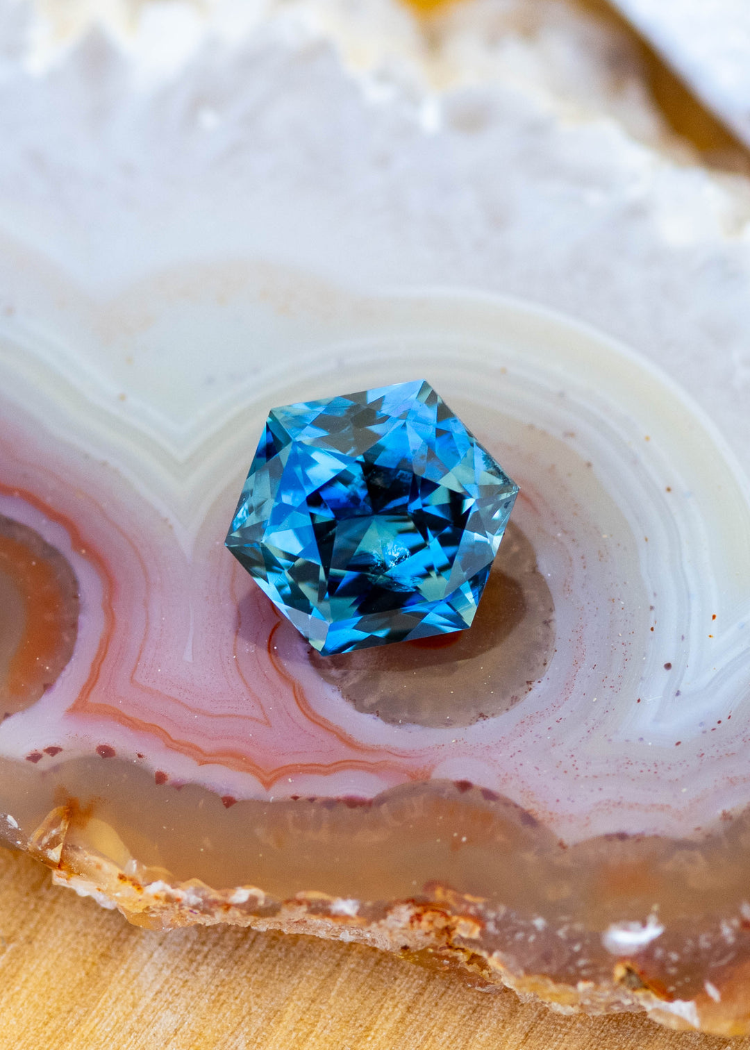 2.03ct blue teal precision hexagonal cut sapphire resting on an agate slice under natural light.