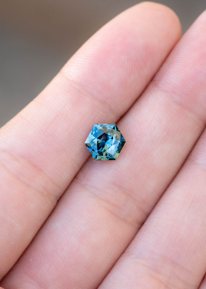 2.03ct blue teal precision hexagonal cut sapphire resting on fingertips to show color and scale.