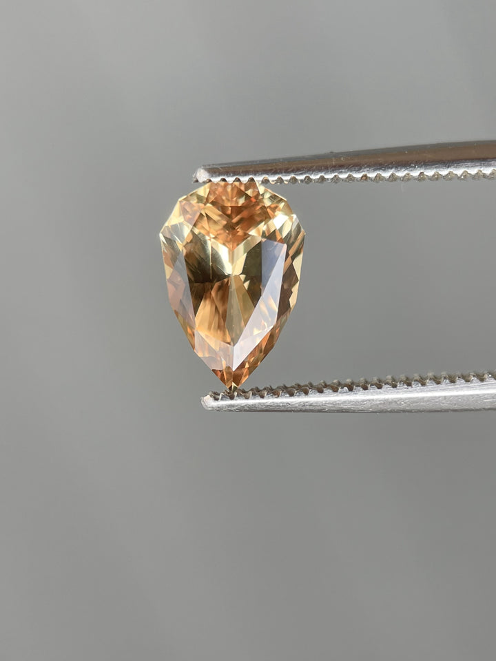 Yellow-Brown Sapphire held by tweezers, highlighting its precision-cut pear shape and golden-brown hues, weighing 2.04 carats.