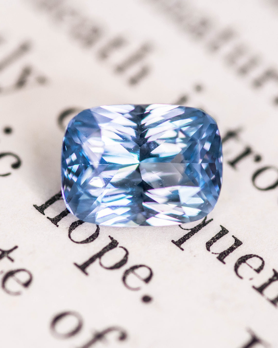 Close-up of a 2.04 carat heated seafoam and blue sapphire on a book page, showcasing precision elongated cushion mixed cut facets and bright internal reflection.
