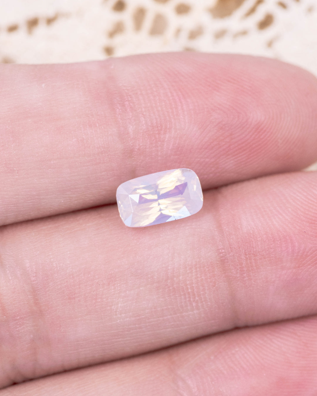 2.05 carat opalescent peach sapphire placed on fingertips under natural light, showing radiant transparency, cushion cut faceting, and untreated origin from Sakaraha, Madagascar.