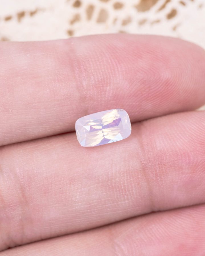 2.05 carat opalescent peach sapphire placed on fingertips under natural light, showing radiant transparency, cushion cut faceting, and untreated origin from Sakaraha, Madagascar.