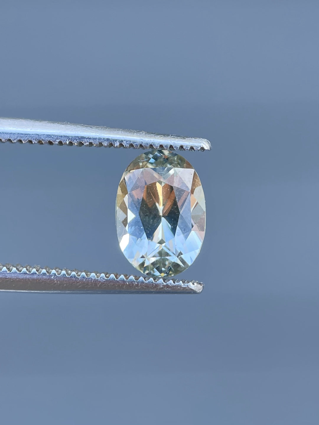 A 2.05-carat gray and yellow sapphire with a mix brilliant oval cut, resting on a fingertip, showcasing its natural sparkle and Sri Lankan origin.