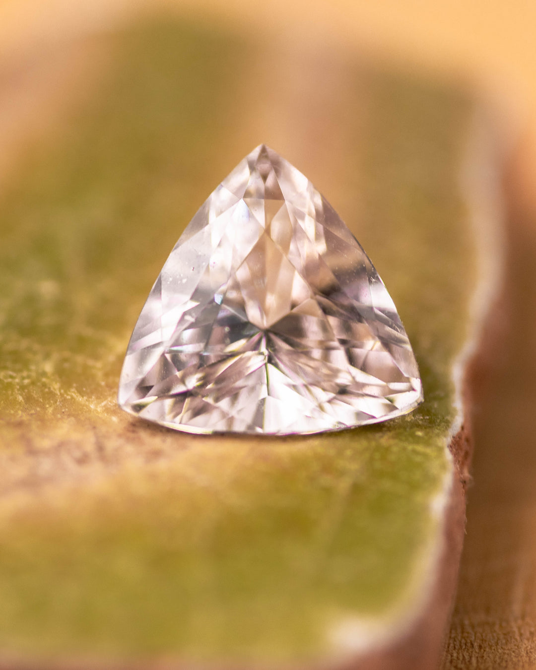 2.06 carat pink and peach sapphire resting on a mossy green surface, displaying vivid brilliance and clean facets of the trillion cut, untreated sapphire from Sakaraha, Madagascar.