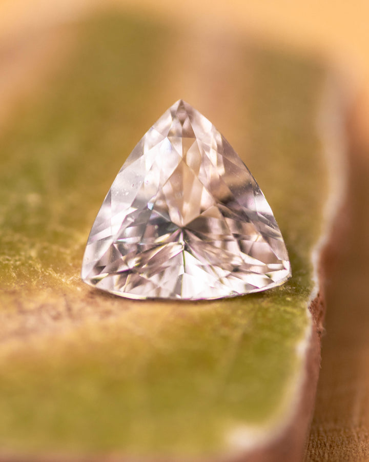 2.06 carat pink and peach sapphire resting on a mossy green surface, displaying vivid brilliance and clean facets of the trillion cut, untreated sapphire from Sakaraha, Madagascar.