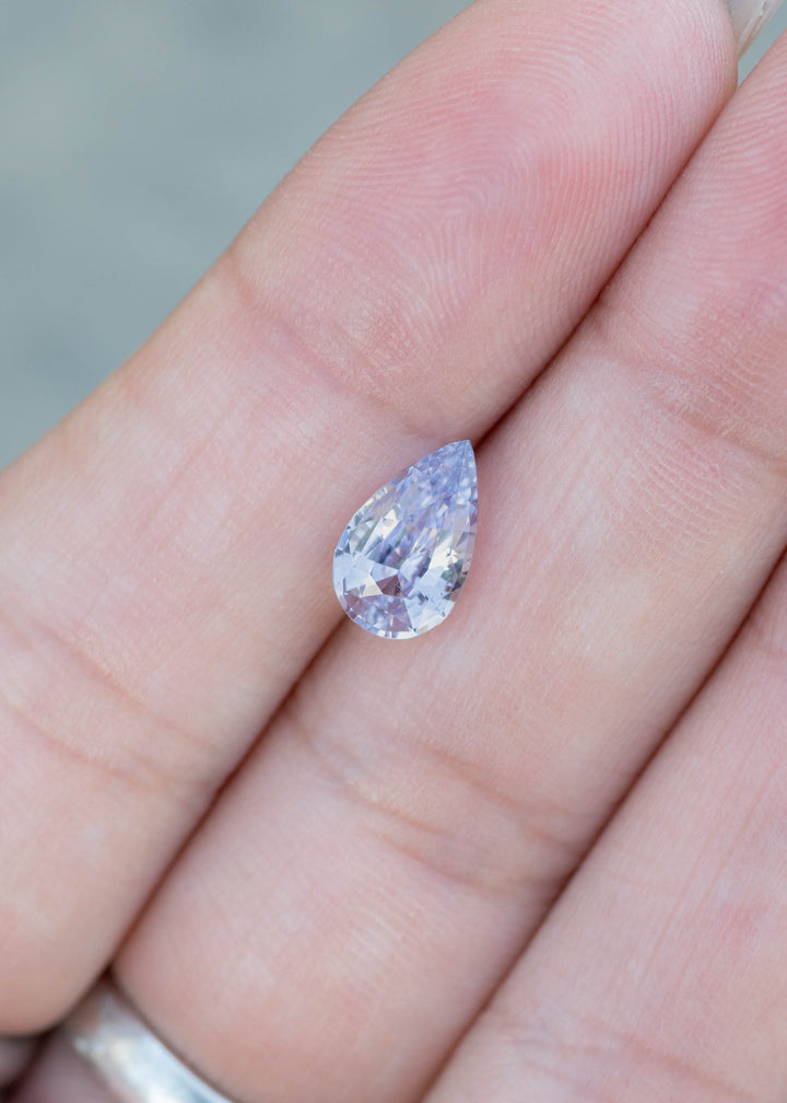 Loose natural lavender pear cut sapphire held in fingers for custom engagement ring design
