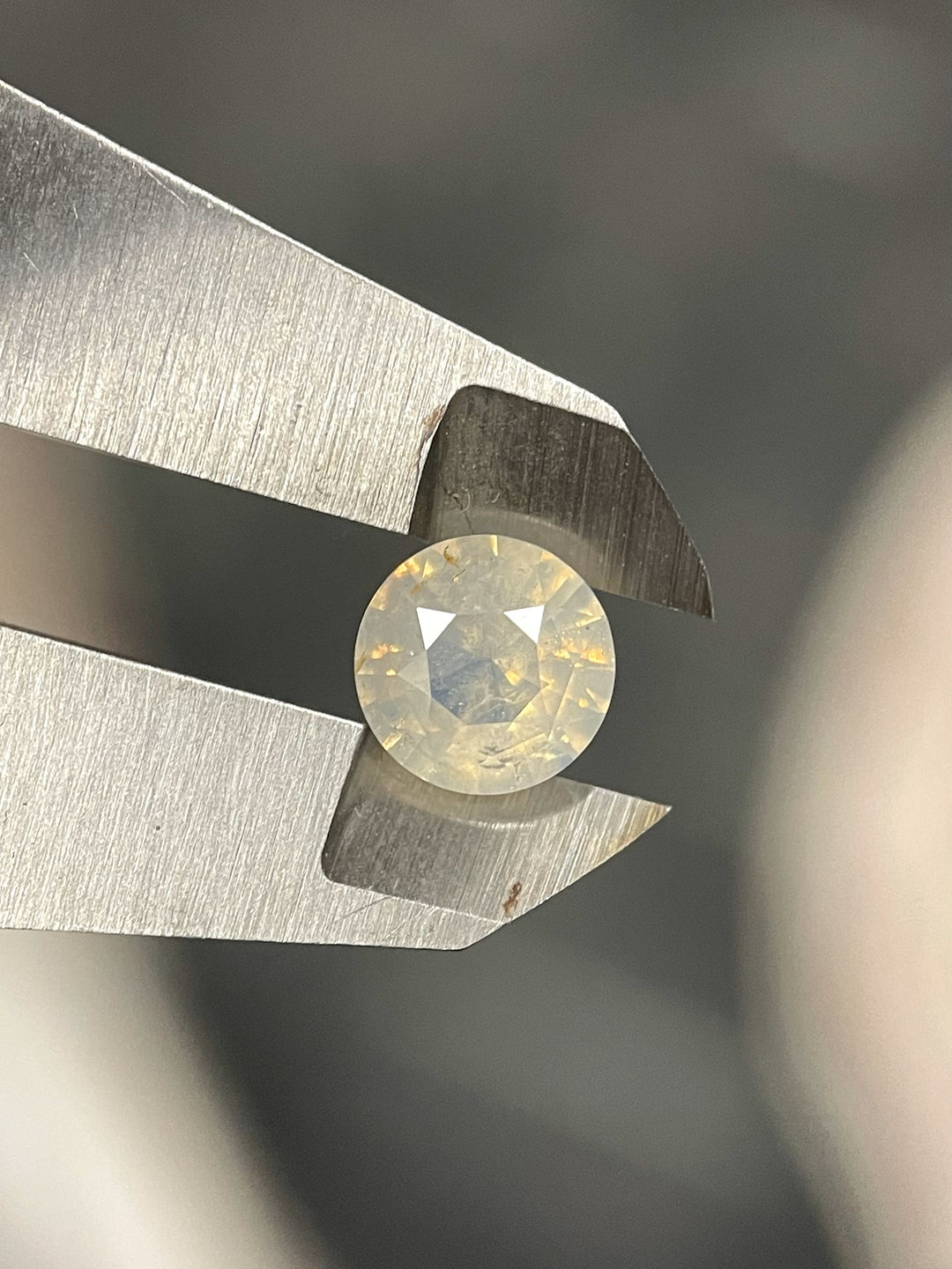 Close-up of a 2.08 carat sapphire gemstone, round brilliant cut, displaying opalescent white to yellow hues, untreated and sourced from Sri Lanka.