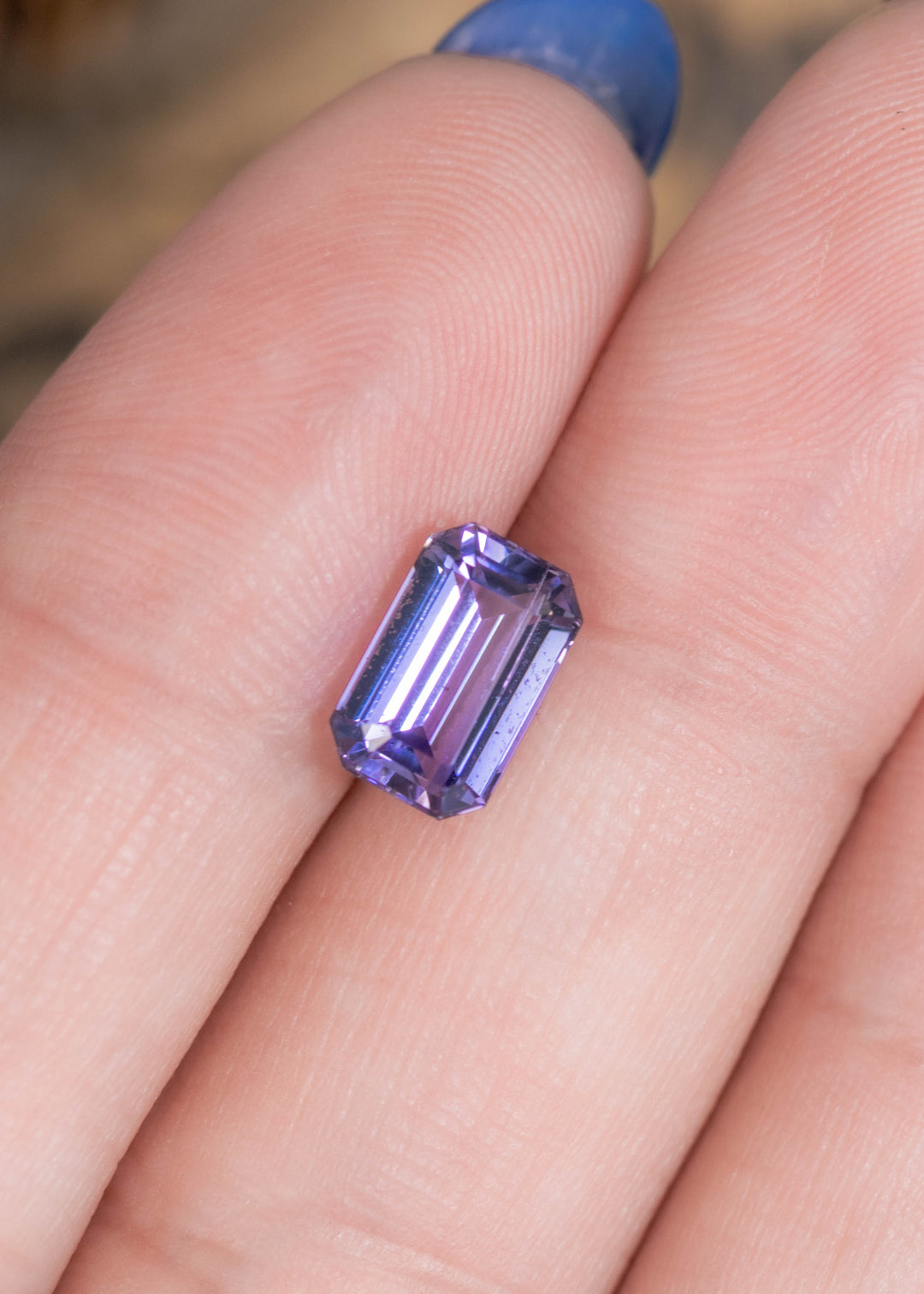 2.08 carat lavender purple Tanzanite octagonal step cut resting on finger, precision faceted untreated gemstone from Tanzania highlighting elongated hall-of-mirrors effect and elegant custom jewelry appeal