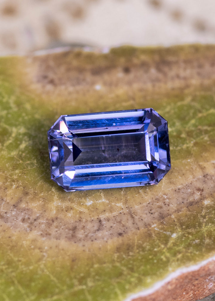 2.08 carat lavender purple Tanzanite octagonal step cut displayed on natural stone surface, untreated Merelani Hills Tanzania gemstone showing long mirrored step facets, beveled corners and vivid violet blue brilliance for custom jewelry