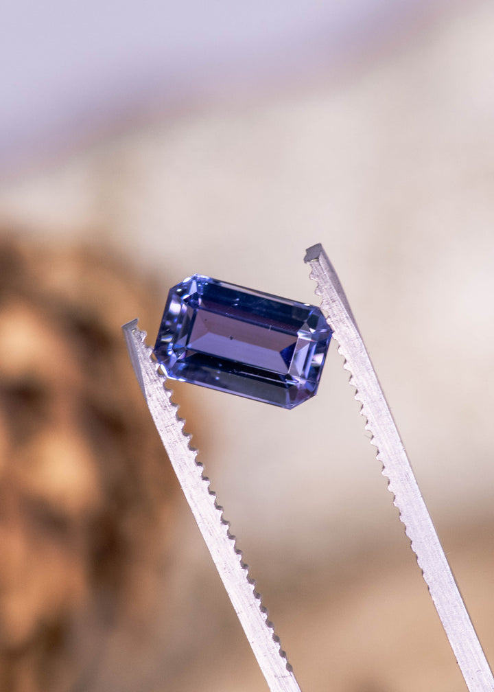2.08 carat lavender purple Tanzanite octagonal step cut held in tweezers, untreated gemstone from Merelani Hills Arusha Tanzania displaying crisp geometric symmetry, clean step faceting and vibrant purple blue flashes for fine jewelry design