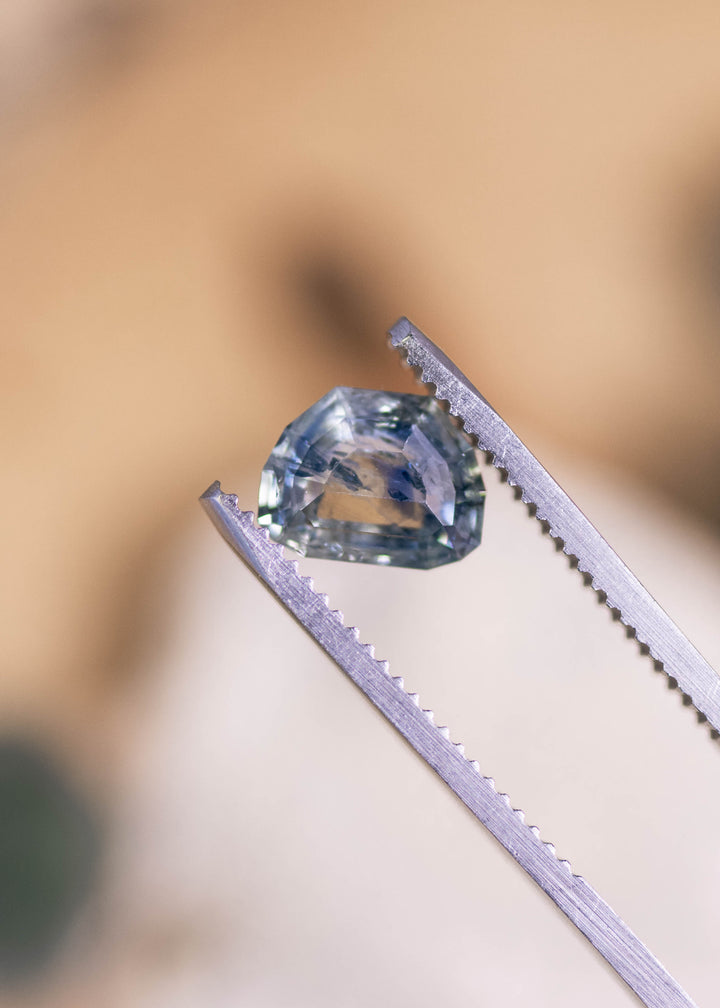 Loose 2.11 carat blue teal sapphire from Montana held in tweezers, showing the geometric tablet cut and crisp facet structure.