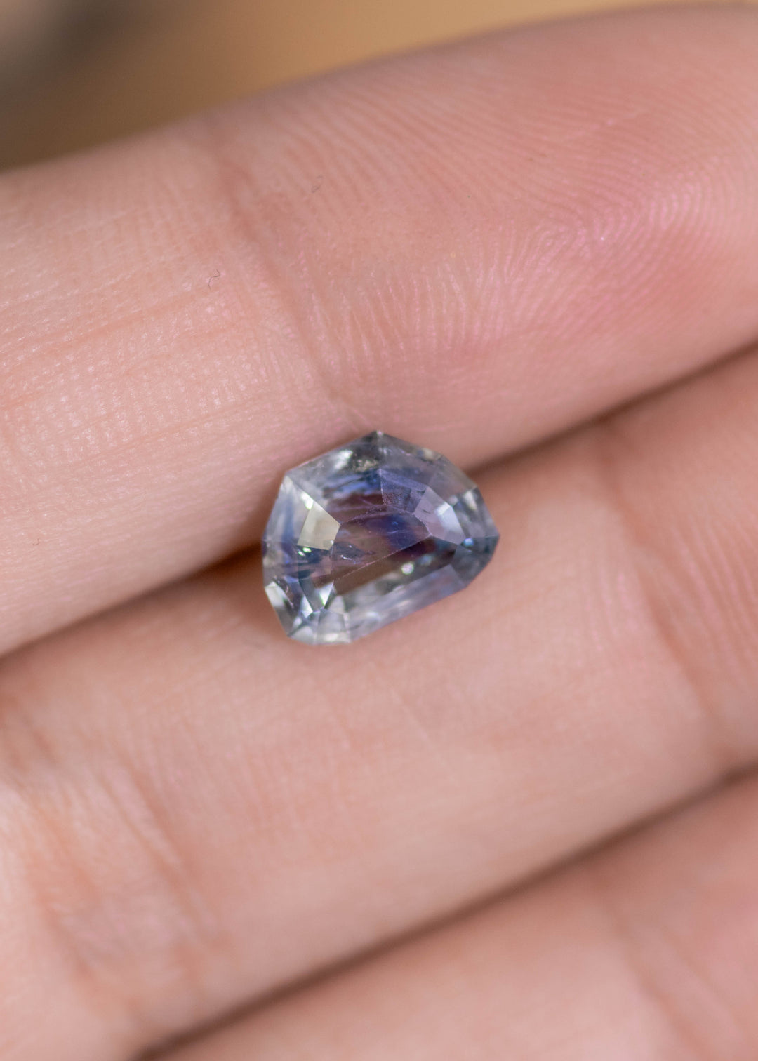 Loose 2.11 carat heated blue teal Montana sapphire resting on fingertips, displaying the geometric tablet cut and natural color zoning.