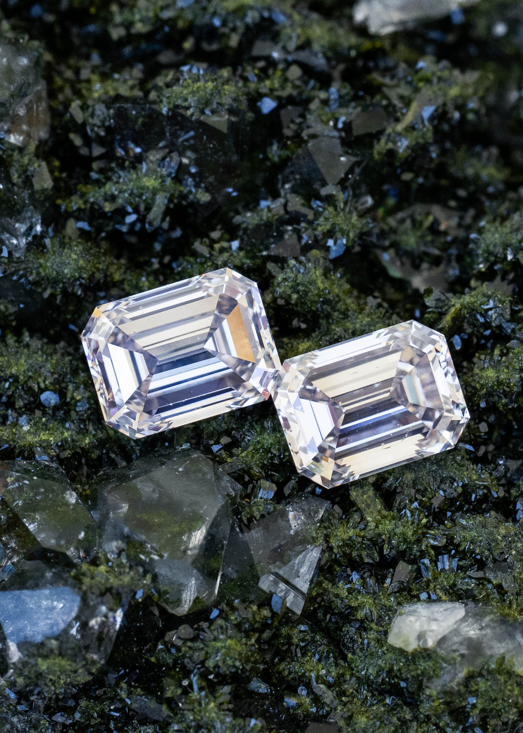 Two light rosy brown emerald cut Canadian diamonds totaling 2.13 carats positioned together on dark green mineral crystals, showing their closely matched proportions and long step facets.