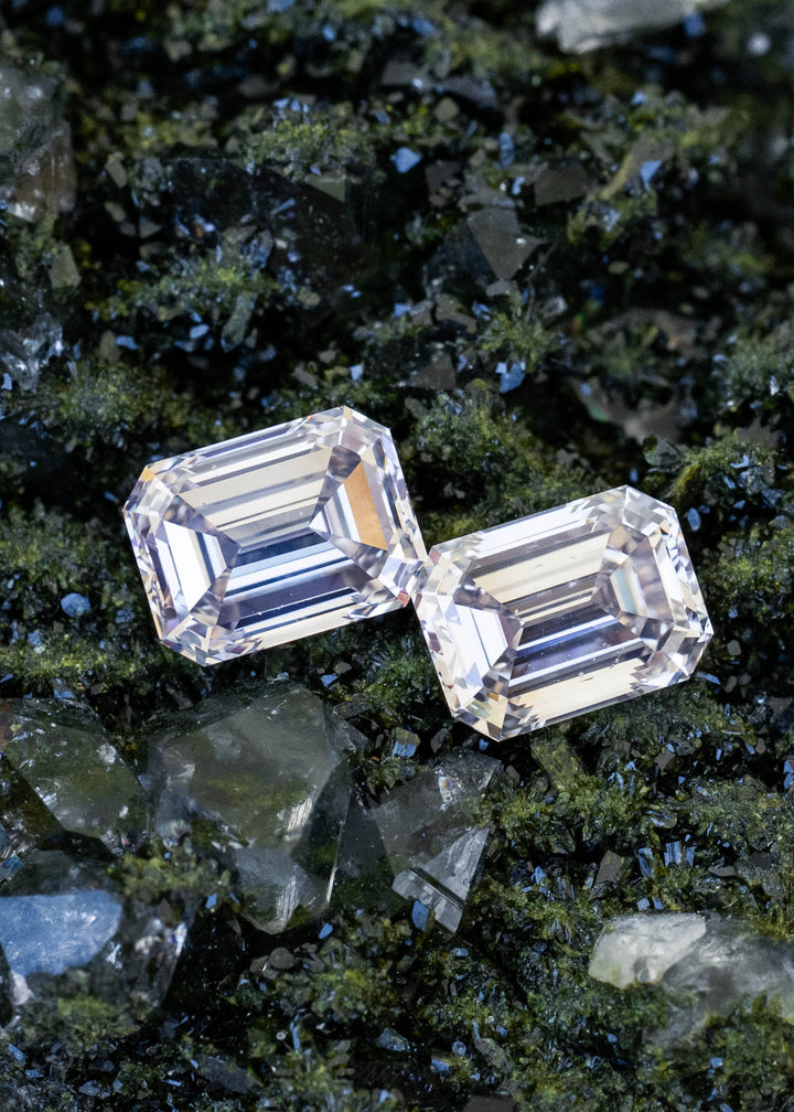 Two light rosy brown emerald cut Canadian diamonds totaling 2.13 carats positioned together on dark green mineral crystals, showing their closely matched proportions and long step facets.