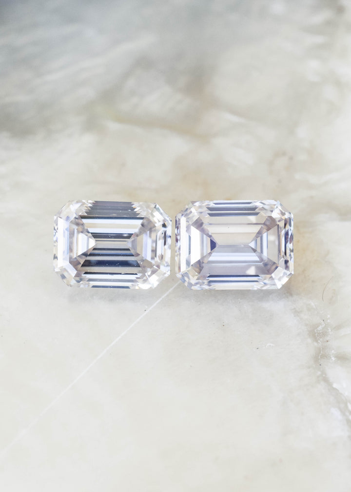 Face-up view of two matched emerald cut Canadian diamonds totaling 2.13 carats on a pale mineral surface, showing their clipped corners, rectangular proportions and parallel step facets.