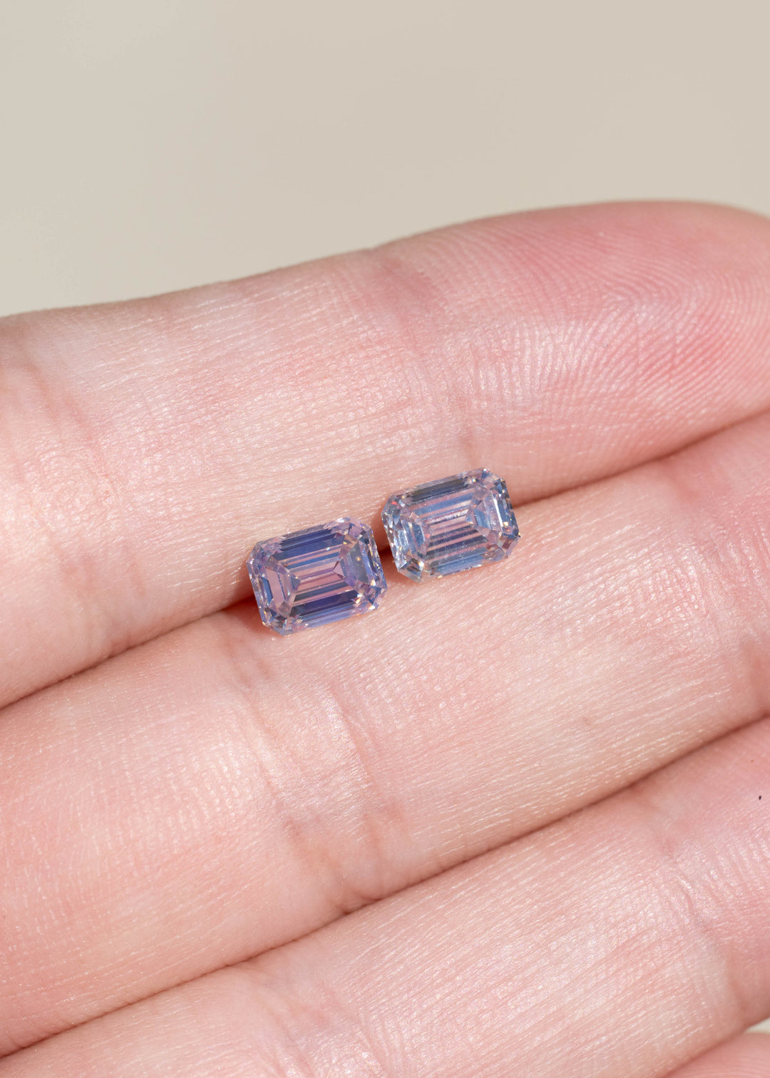 Matched pair of natural Canadian emerald cut diamonds resting side by side on a hand, displaying their subtle rosy brown color, VVS clarity and elongated rectangular shapes.